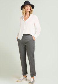 Blusa blanca con escote en v y mangas largas, combinada con pantalones grises de corte entallado y zapatillas deportivas plateadas. Un sombrero oscuro de fieltro completa el conjunto.