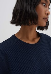 Top in jersey texturato blu navy con scollatura rotonda, caratterizzato da un delicato motivo a griglia. È evidente che ha maniche corte e una vestibilità rilassata.