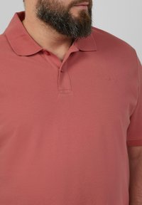 Korte mouwen polo shirt in stoffige roos, gemaakt van gestructureerde stof. Bevat een kraag en een klein logo op de borst.