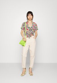 Camisa floral com frente amarrada, predominantemente verde, rosa e amarelo; combinada com calças creme, sandálias de salto bloco verdes e uma pequena bolsa verde.