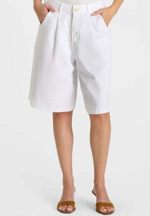 Weiße Shorts mit hoher Taille bis zum Knie, vorne mit Falten und Taschen, getragen mit braunen offenen Sandalen an einer stehenden Person.