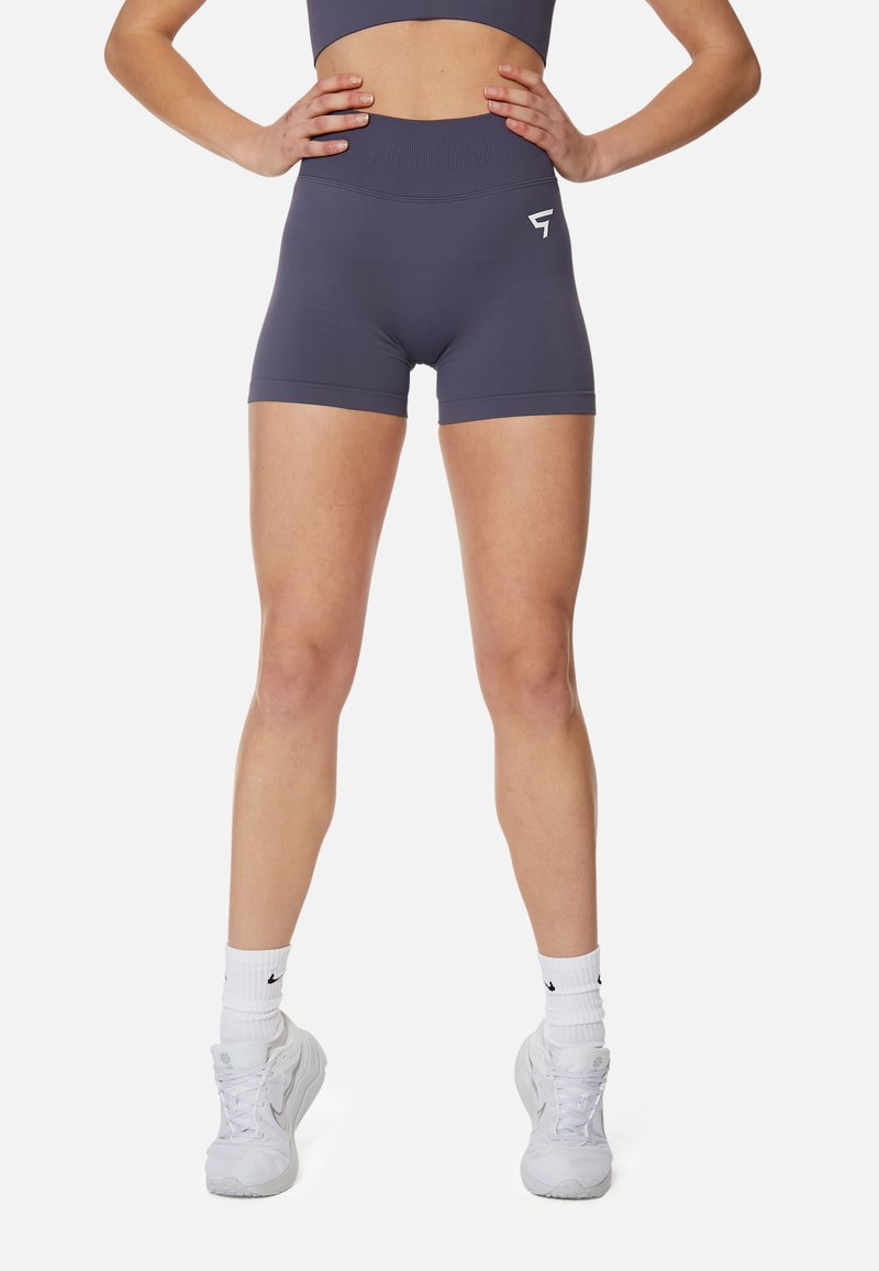 Šedé atletické šortky vyrobené z elastického materiálu, s vysokým pásom a logom na prednej strane. Nosené s bielymi teniskami a ponožkami.