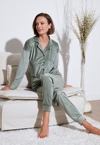 Set de pijama de terciopelo verde, que incluye una camisa de botones con cuello y mangas largas, combinada con pantalones a juego. Textura suave y corte relajado.