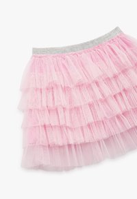 Rosa Tüllrock mit geschichteten Rüschen, versehen mit einem silbernen elastischen Bund. Weicher, transparenter Stoff mit mehreren Lagen für Volumen.