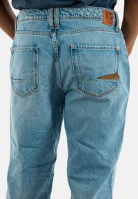 Vaqueros de mezclilla azul claro de cintura alta, con bolsillos traseros, costuras en contraste y una etiqueta de cuero marrón en la cintura.