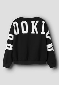 Sudadera negra con grandes letras blancas que dicen "BROOKLYN" en la parte trasera y las mangas, exhibida sobre un fondo gris.