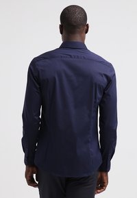 Mörkblå skjorta med knappar och lång ärm, standardkrage, bakveckdetalj och figursydd design. Tillverkad av mjukt, lätt tyg.