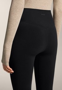 Leggings noires taille haute en tissu lisse et extensible. Dotés d'un logo à l'arrière et d'une coupe ajustée qui met en valeur la taille.
