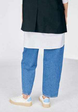 Jean large en denim bleu associé à une chemise longue blanche, complété par des baskets blanches avec des accents bleu clair.