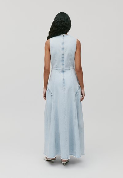 Robe maxi en denim bleu clair, avec un corsage ajusté, sans manches, et des bords effilochés subtils, dotée d'une fermeture éclair au dos.