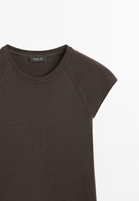 Top corto a maniche corte di color marrone scuro, con scollatura rotonda e maniche raglan. Realizzato in tessuto morbido con una leggera texture. Etichetta del marchio visibile sul collo.