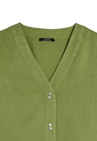 Zielona, krótka koszula z guzikami z dekoltem w kształcie litery V. Charakteryzuje się gładką fakturą i czterema guzikami z przodu, z wyszywanymi detalami.