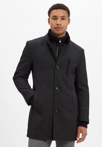 Schwarzer Mantel mit strukturiertem Design, texturiertem Stoff und hohem Kragen. Mit Reißverschluss, Knopfverschluss und Seitentaschen ausgestattet.