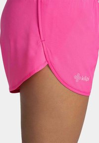 Lyserøde træningsshorts med split kant og blød tekstur, som har et hvidt logo nederst til højre for branding.