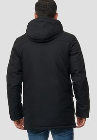 Parka noire avec capuche, en tissu lisse et texturé. Le design comprend une coupe robuste et des détails de couture simples.