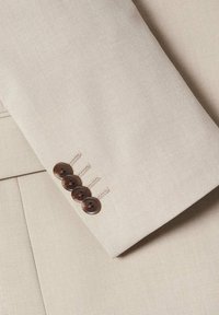 Beige blazer mouw met vier donkerbruine knopen, voorzien van een gladde stoftextuur en subtiele stikdetails. Classiek op maat gemaakt ontwerp.