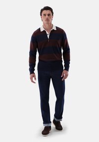 Pullover in Marineblau und burgunderfarbigen Streifen mit einem weißen Kragen, ausgestattet mit einem Rippenbund. Kombiniert mit dunklen Jeans und brauen Schuhwerk.