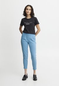 T-shirt en coton noir avec le texte "gosse d'amour", associé à un pantalon léger sur mesure de couleur bleu clair et des mocassins noirs. Tissu lisse et design ajusté.