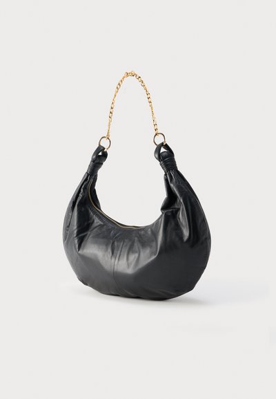 Sac bandoulière en cuir noir avec poignée chaîne dorée et fermeture éclair, avec des lanières nouées aux extrémités de la poignée.