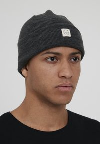 Dark gray knit beanie with a ribbed texture and a small white logo patch, fitting closely on the head.