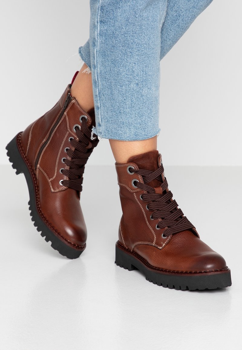 Bruna läderankelboots med texturerad yta, featuring kontrasterande mörka snörningar, sidodedragkedja och chunky svart gummisula.