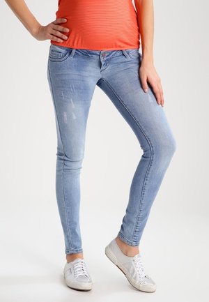 Jeans skinny de mezclilla azul claro con detalles sutiles desgastados, cintura baja y bolsillos frontales, combinados con zapatillas plateadas.