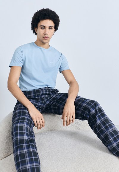 Tricou bleu deschis cu mânecă scurtă și guler rotund, asortat cu pantaloni de lounge bleumarin cu model în carouri, așezat pe o suprafață texturată.