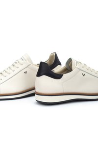 Zapatillas de cuero blanco con tacón de cuero negro. Presentan cordones ligeros, un forro gris y un acento en la suela marrón. Logos de la marca discretos en un lateral.