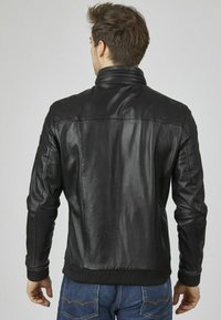 Chaqueta de cuero negro con cuello con cremallera, puños acanalados y un acabado suave. Presenta un diseño ajustado y detalles de costura sutiles.