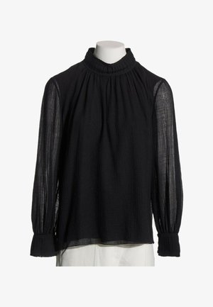 Blouse noire à manches longues en tissu transparent texturé, col montant à volants et poignets ajustés, présentée sur un mannequin sans tête.