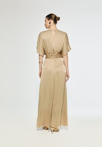 Beige satin long dress with a cinched waist, flutter sleeves, and a keyhole back detail. Sheer texture and flowing design with a maxi length.