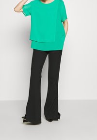 Top in chiffon verde con un design a strati, abbinato a pantaloni a zampa neri e tacchi a punta. Texture liscia con una vestibilità comoda.