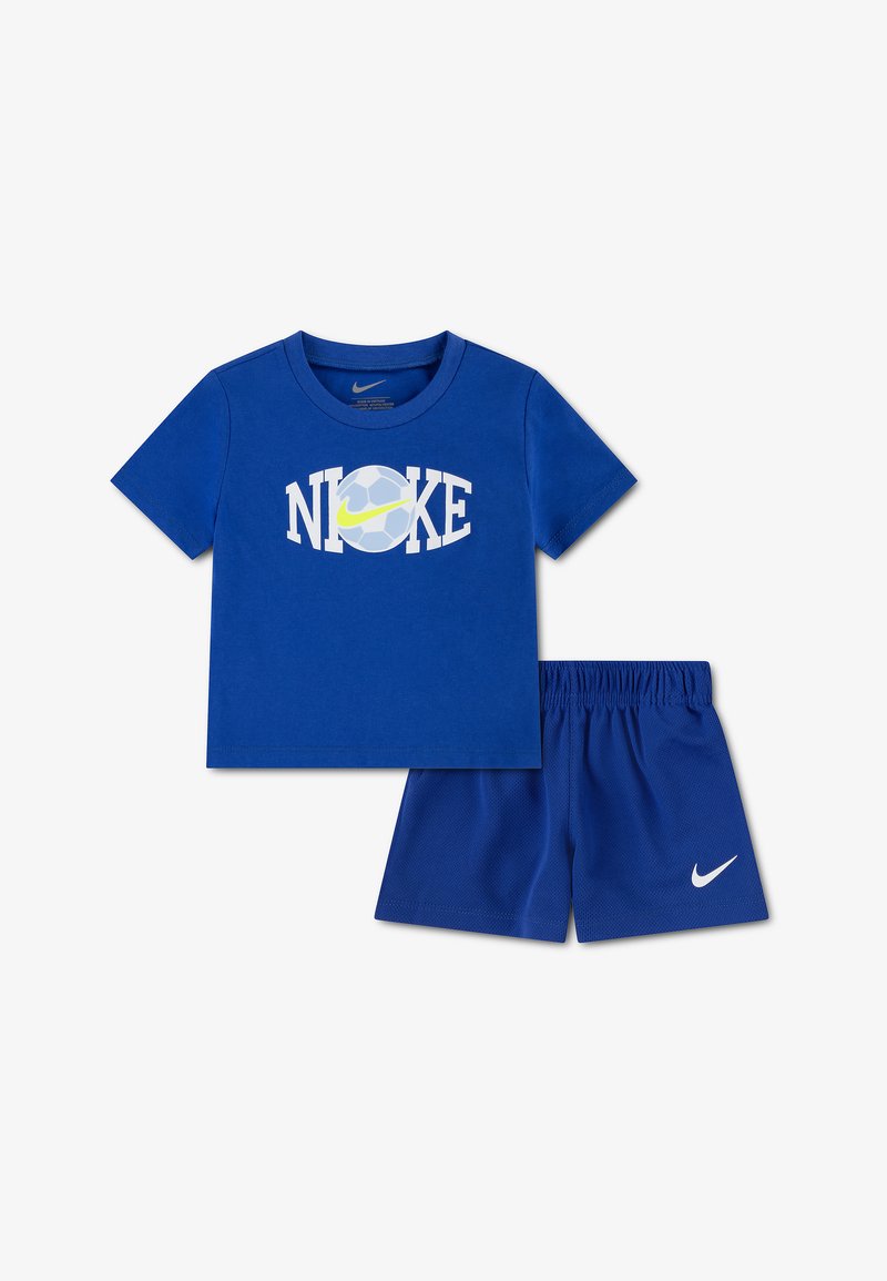 Μπλε παιδική στολή Nike με κοντομάνικο πουκάμισο που έχει λογότυπο ποδοσφαιρικής μπάλας και swoosh, σετ με μπλε σορτς με λευκό λογότυπο swoosh.