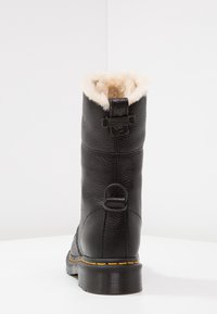 Stivale in pelle nera invernale con fodera in pelliccia beige, con linguetta posteriore e cuciture gialle sulla suola in gomma spessa, mostrato da una vista posteriore.