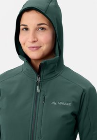 Felpa con zip di colore verde scuro realizzata in tessuto testurizzato, dotata di cappuccio e di un piccolo logo sul petto. La cerniera presenta un tirante di contrasto.