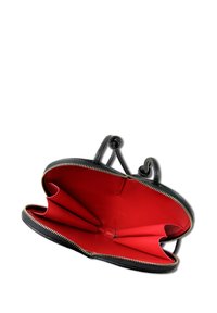 Zwarte leren handtas met een rode binnenkant. Heeft een ritssluiting, twee compartimenten en gebogen handvatten. Gladde textuur en minimalistisch ontwerp.