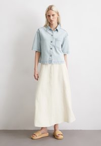 Light blue denim short-sleeve shirt with front pocket, cream-colored linen maxi skirt, and tan woven slide sandals. Simple, relaxed design.