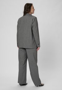 Costumul gri cu dungi are un sacou croit și pantaloni evazați. Textură netedă, cu rever decupat și butoane decorative pe mâneci.
