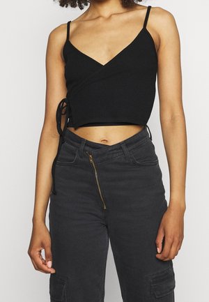 Top court noir à côtes avec des bretelles spaghetti et un design enroulé, agrémenté d'un détail de lien sur le côté. Associé à un pantalon gris foncé taille haute.