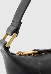 Zwarte leren handtas met een gladde textuur, voorzien van een ritssluiting en riembevestiging in goudkleurig metaal. Geaccentueerd met merkdetails.