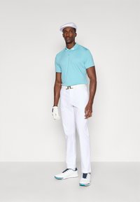 En teal polo skjorte med hvit krage, hvite bukser og hvite golfsko med blå aksenter. En hvit caps og hanske fullfører antrekket.