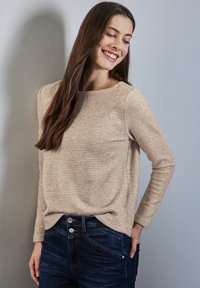 Maglietta a maniche lunghe a righe beige con collo rotondo, realizzata in tessuto morbido, abbinata a jeans in denim scuro con dettagli sui bottoni.
