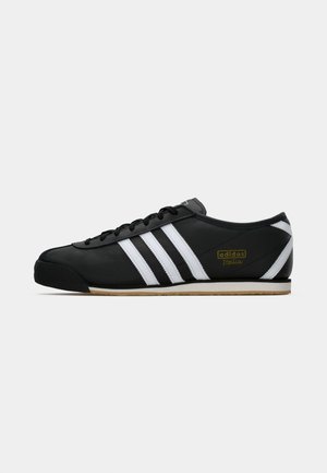 Schwarzer Adidas Italia Sneaker mit weißen Streifen, Gummisohle, schwarzen Schnürsenkeln und goldenem Logo an der Seite, im Profil auf einem weißen Hintergrund dargestellt.