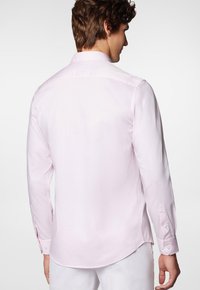 Jasnoróżowa koszula z długim rękawem, z kołnierzykiem typu point, guzikami przy mankietach i zaokrąglonym dołem. Gładka tekstura i dopasowany krój.