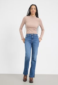 Helles, strukturiertes, langärmliges Oberteil in Rosa mit einem Rüschensaum, kombiniert mit hochtaillierten blauen Jeans mit geradem Bein und seitlichen Schlitzen.