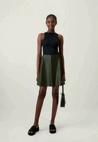 Top preto sem mangas, saia esvoaçante verde oliva, sandálias de plataforma pretas e uma pequena bolsa preta. Texturas suaves, design ajustado, comprimento até ao joelho.