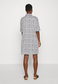 Robe à manches courtes avec un motif à pois noir et blanc, dotée d'un col, à coupe ample et atteignant le mi-thigh. Tissu texturé, design minimaliste.