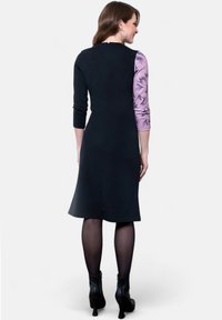 Mustat mekko, jossa on tiukka leikkaus, kolmanneksen pituiset hihat, joissa on vaalean violetin kukkakuosi, ja nilkkurit.