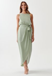 Dolga, brezrokavna maksi obleka v pastelnem zeleni satenu. Ima pas z vezavo, tekočo silhueto in stranski razporek za dodatno gibljivost.