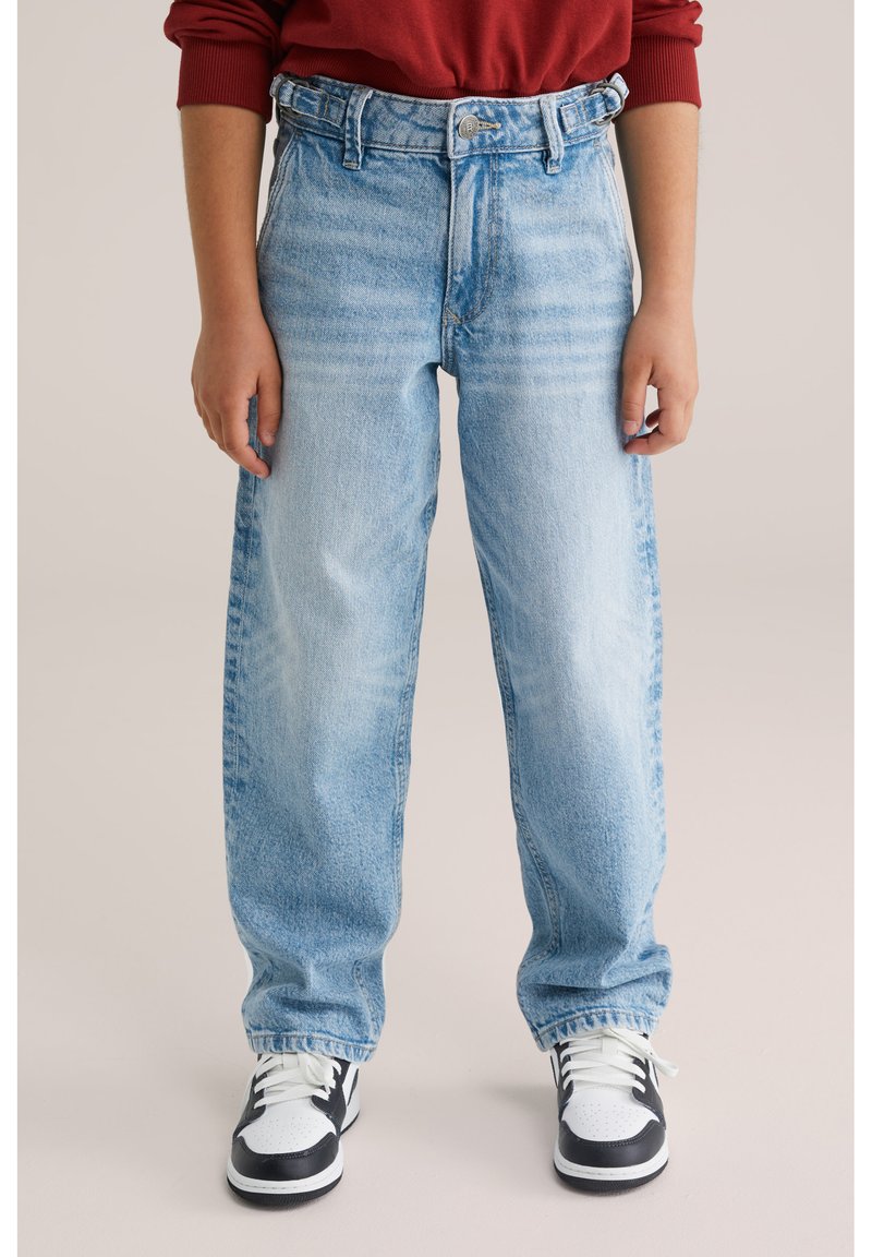 Jeans in denim leggero blu con una vestibilità ampia, vita alta e motivo sbiadito. Abbinati a scarpe da ginnastica bianche e nere.